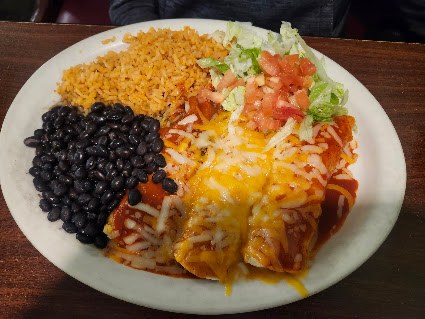 A combination plate with rice, black beans and enchiladas