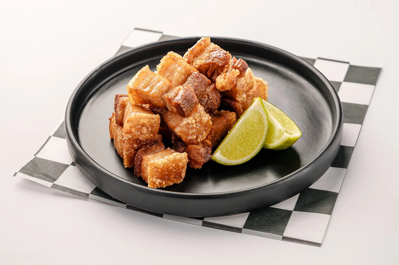 Crisp bites served with lime on a black plate.